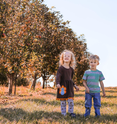 Two siblings grinning ear to ear as they play in an orchard enjoying each other's company.