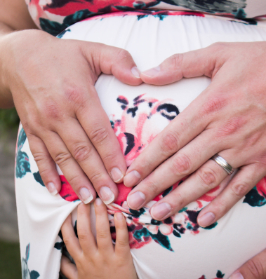 A mother-to-be cradling her growing belly while her son gently touches it with love and curiosity.