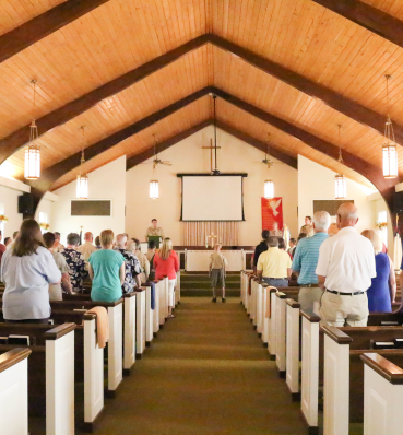 A solemn boy scout ceremony taking place in a church, viewed from the end of the aisle with the focus on the central boy receiving his honors.