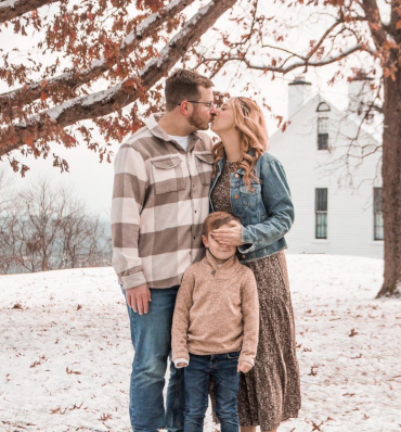 A sweet moment between a couple, stealing a kiss while playfully covering their young son's eyes.