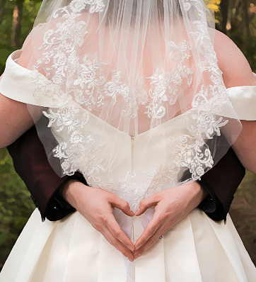 Two hearts united as one: Groom's hands form a heart around the beautiful bride's veil